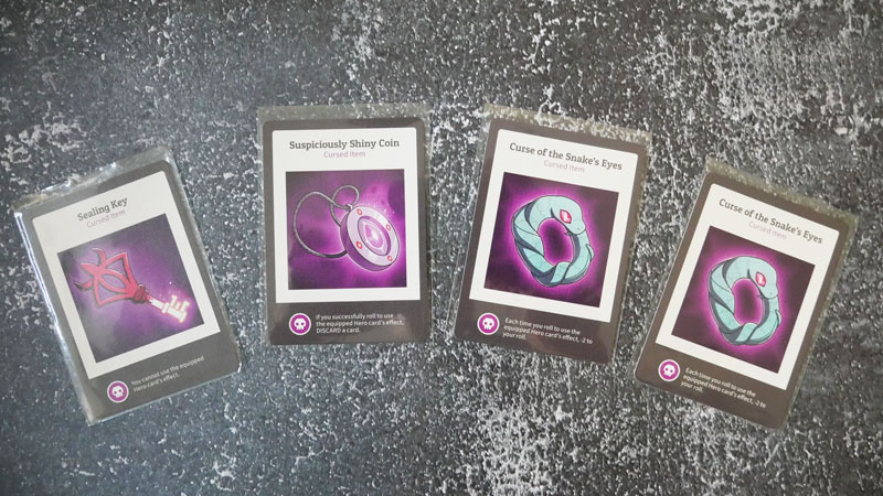 here to slay photo of the 4 cursed item cards on a grey background