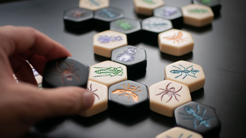 hive board game tiles on a table and a hand placing another piece